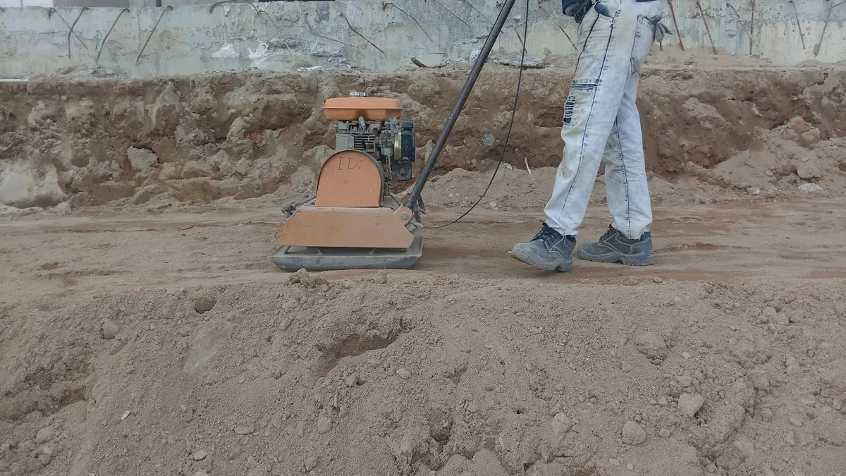 Worker using a plate compactor on a dirt embankment